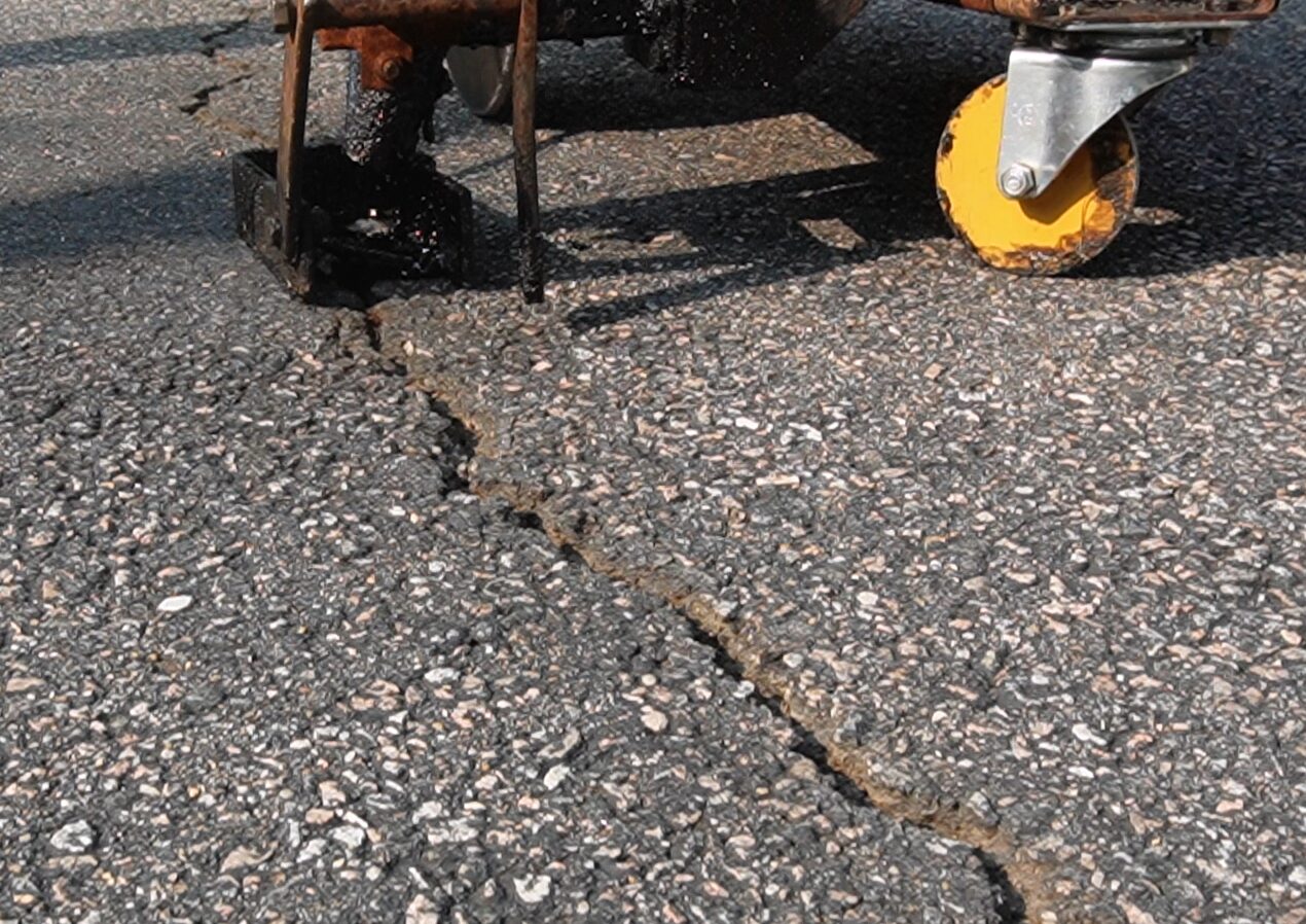 Cleaning debris and vegetation from asphalt cracks before crackfilling